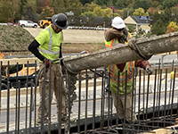 Workers guide cement flow onto abutment base.
